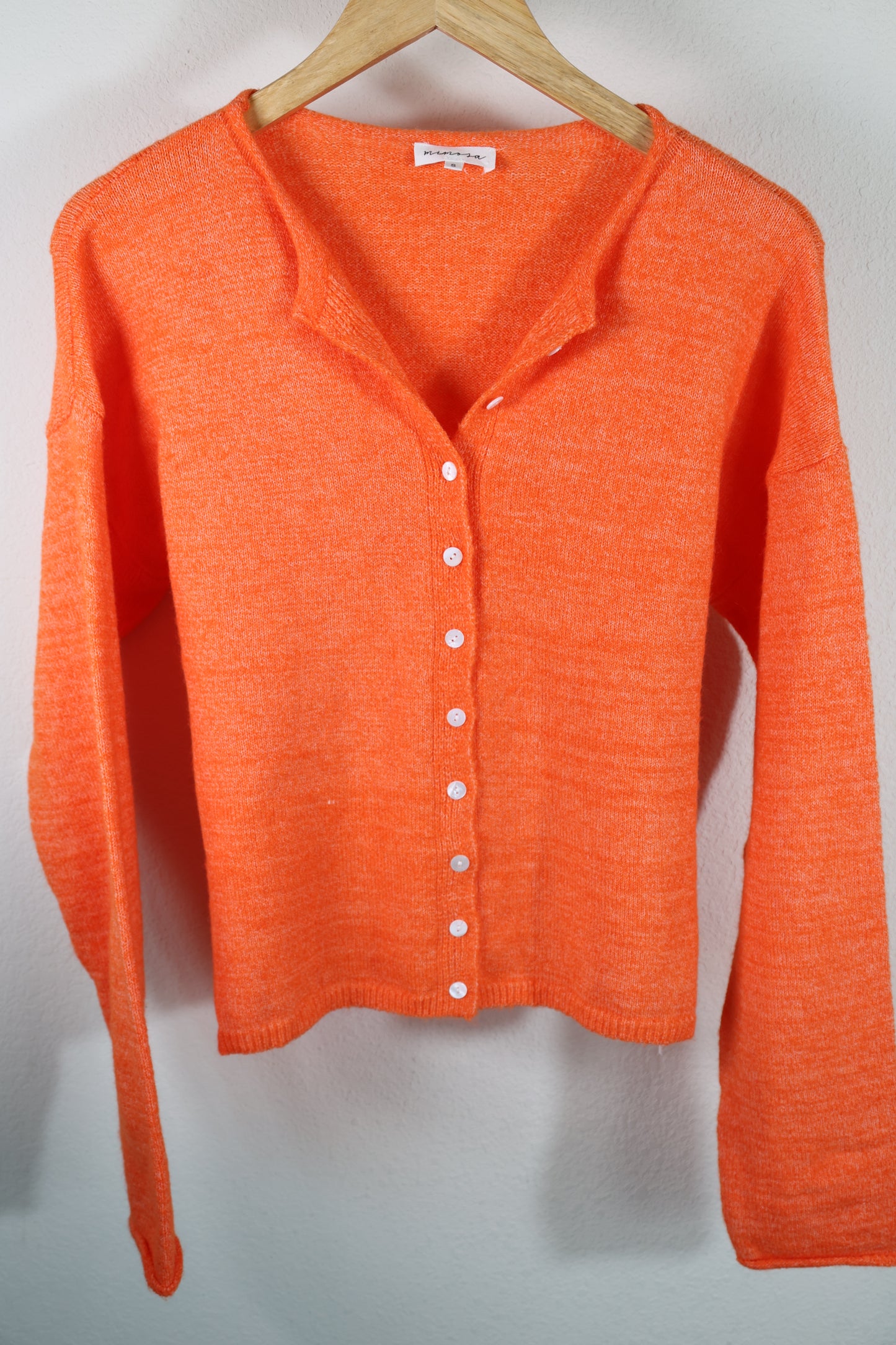 Orange button front cardigan with white buttons on a wooden hanger against a light gray background