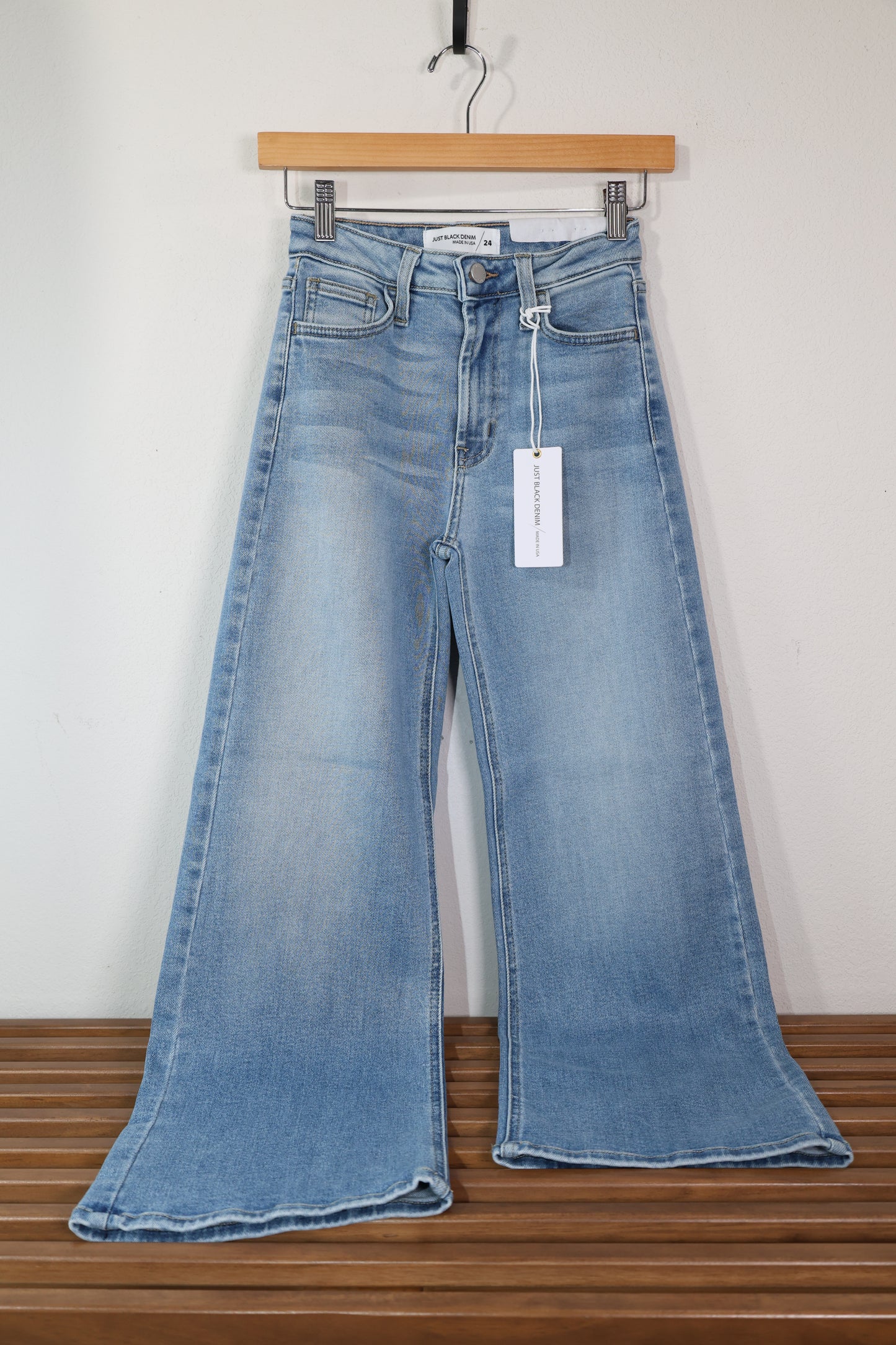A casual pair of jeans shown displayed on a wooden hanger, the jeans are a light wash blue jean with a slim wide leg and finished hem, the wash is perfect for spring 