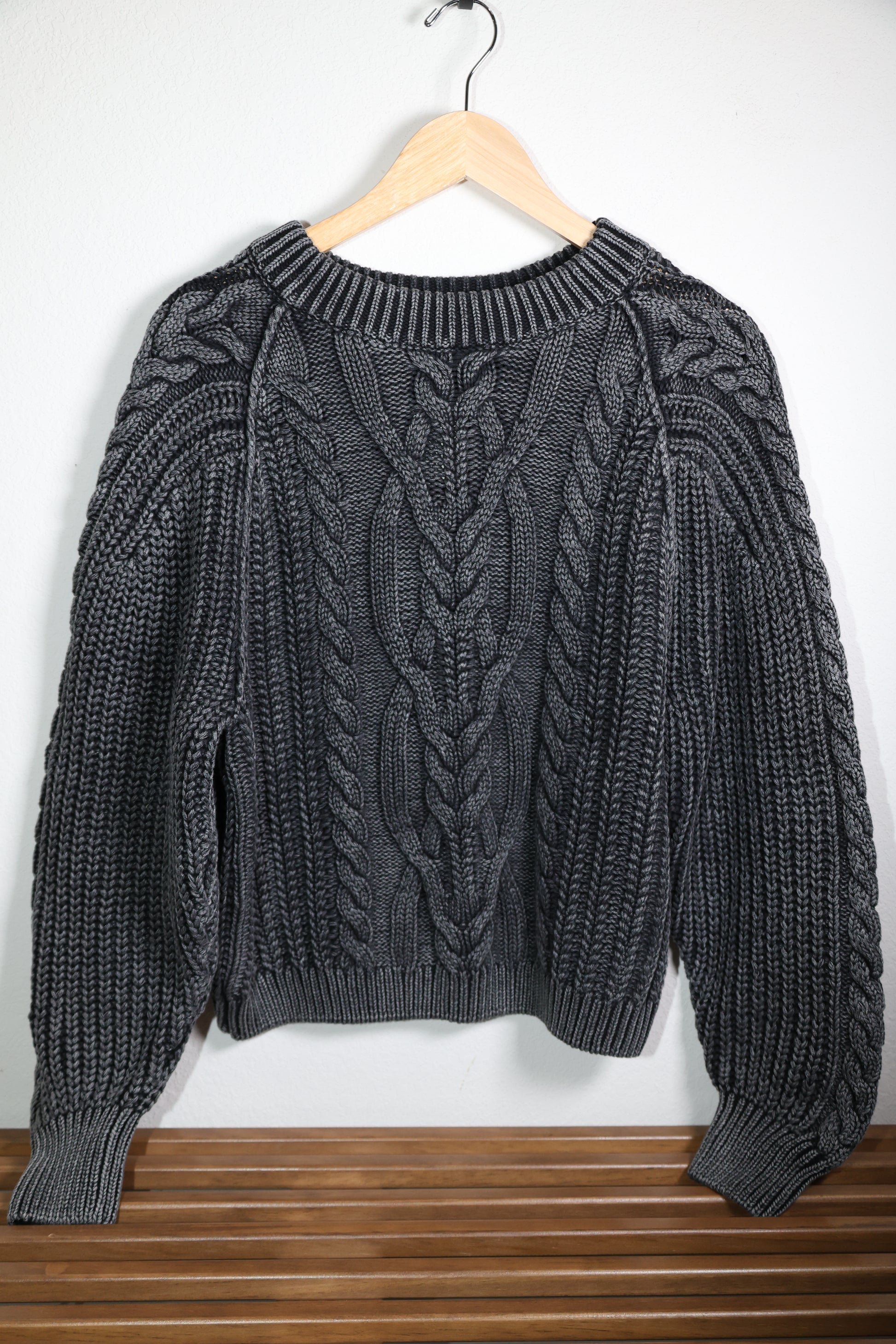 Free People Black cable knit sweater on a wooden hanger against a white background